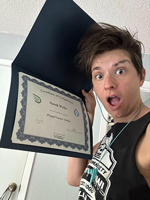 Sarah holding up her Drupal Career Online certificate with a shocked expression on her face.